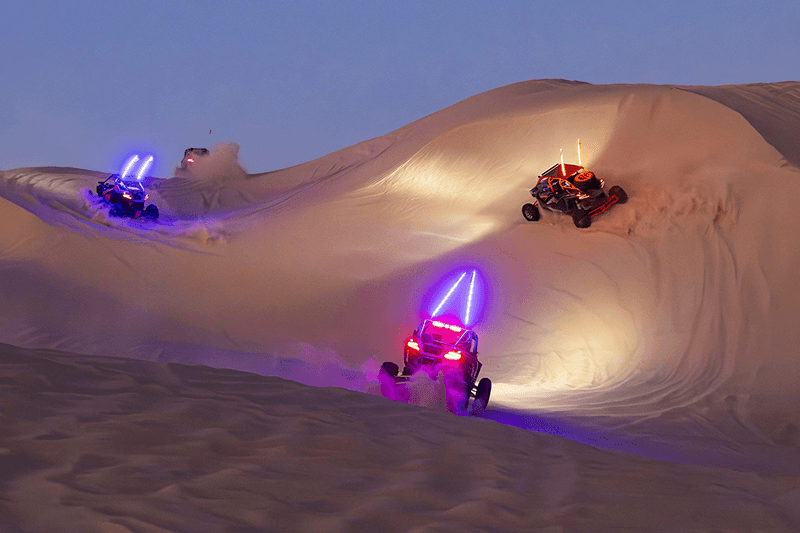 Side-by-sides with illuminated whip flags on the dunes at dusk