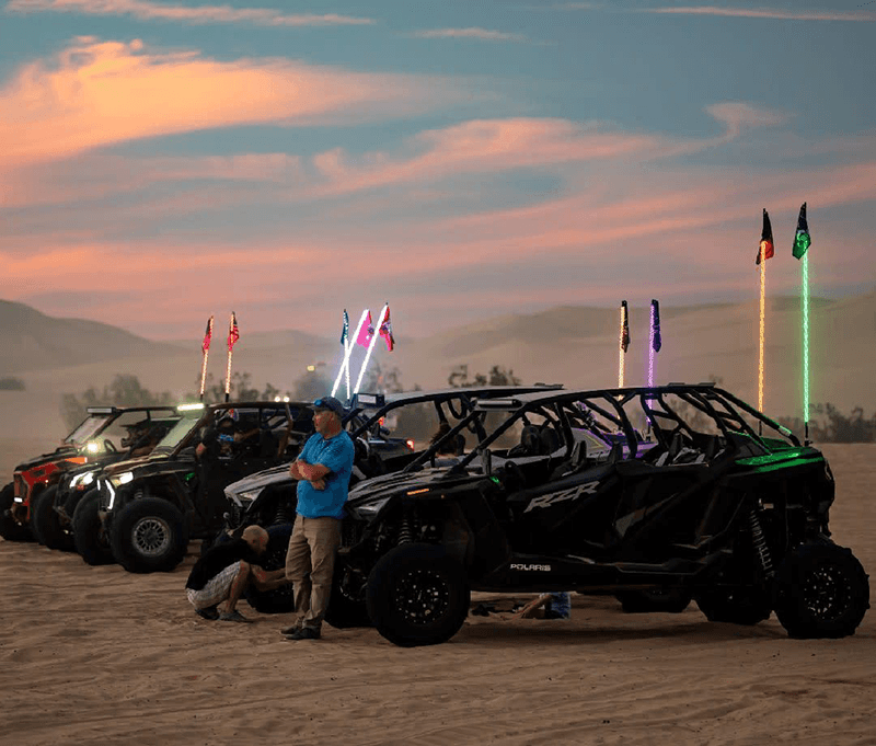 Riders beside parked side-by-sides under an evening sky